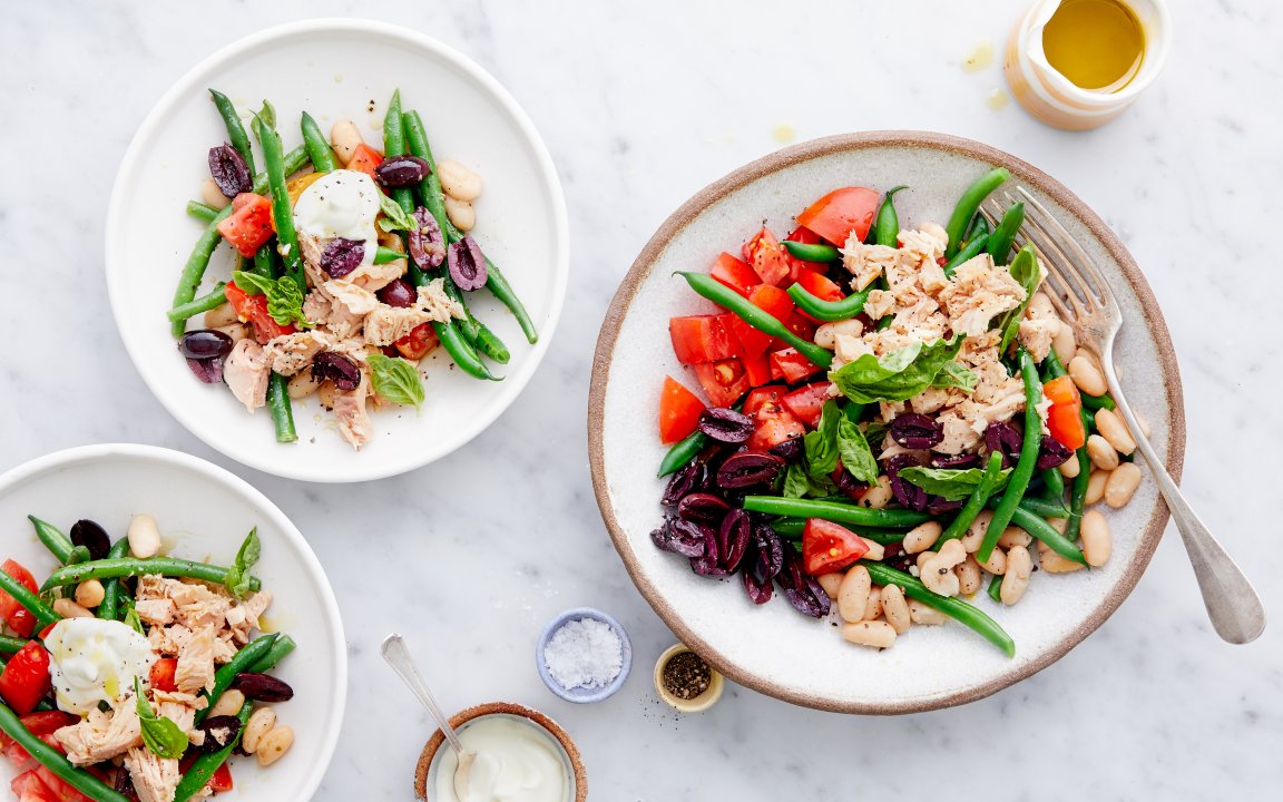 Colorful salad with tuna, green beans, tomatoes, olives, and beans on a white plate, showcasing fresh and healthy ingredients, perfect for a light meal.
